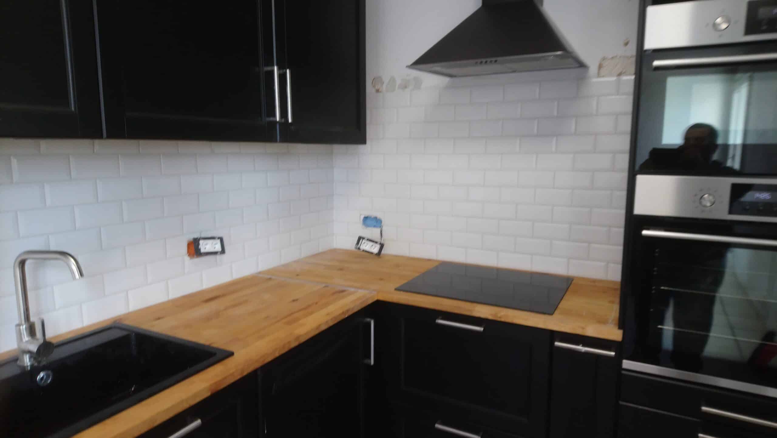 Cuisine moderne avec placards noirs, plan de travail en bois, crédence métro blanche et plaque à induction.