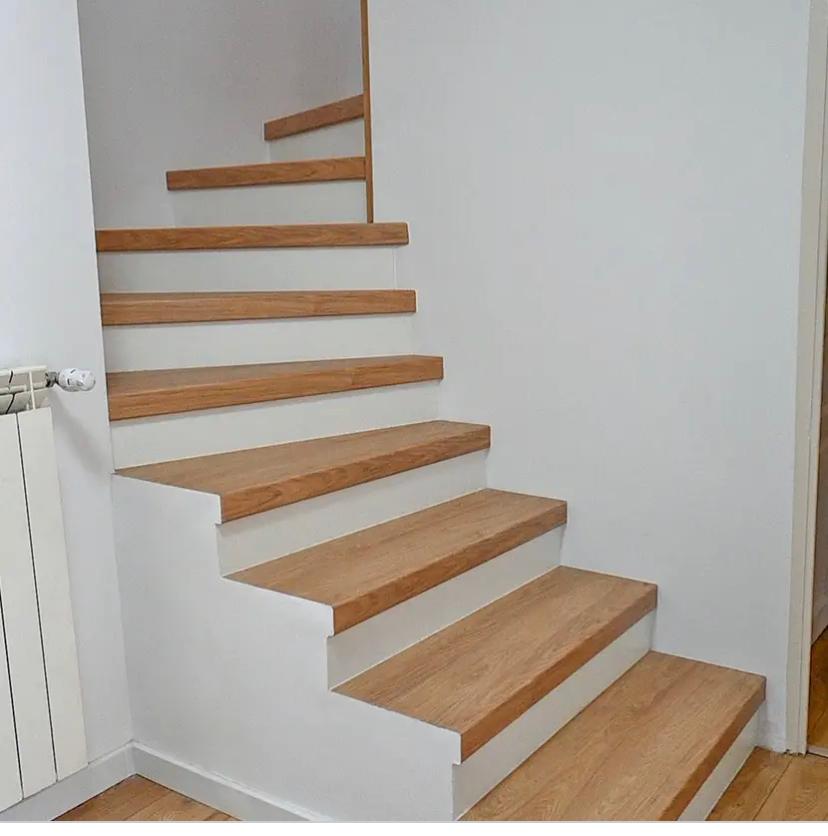 Escalier moderne en bois et blanc dont les marches supérieures se transforment en fines lattes murales décoratives.